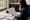 Woman reviews paperwork at a kitchen table beside an open laptop and coffee mug.
