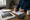 Person reviews paperwork and writes at a table beside a calculator, house photos, and coffee.