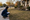 Person kneels beside a suburban lawn, measuring its edge with a tape measure.