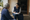Two women sit outside a doorway, conversing as one writes notes on a clipboard.