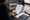 Person reviews a printed document at a wooden desk beside notebooks, coffee, and a window.