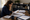 Woman reviews printed documents at a desk surrounded by paperwork in a home office.