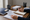 A person writes in a spiral notebook while reviewing printed documents at a wooden desk.