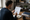 Man reviews a printed checklist beside an open notebook at a desk, with bookshelves and coffee nearby.