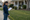 A woman measures a front lawn with a tape measure and clipboard beside marked boundaries.