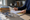 Person reviewing paperwork at a desk beside a stethoscope, folders, and notebooks in a sunlit office.