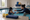 Swim instructor reaches toward a child practicing with a kickboard in an indoor pool.