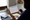 Person reviews a printed document and writes notes at a kitchen table beside notebooks and a mug.