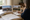A woman studies home photos, a map, and notes at a dining table.