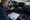 A man examines dashboard wiring while referencing a schematic inside a vehicle, with tools arranged nearby.