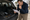 Man examines paperwork beside an open SUV trunk filled with speakers, amplifier, cables, and tools.