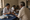 A person in a white coat examines a seated man's hand beside test materials indoors.