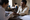 Healthcare worker examines a man's hand at a clinic table while another person writes in the background.