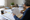 Person reviews printed documents and writes notes at a desk surrounded by paperwork.
