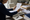 Person reviews printed documents at a desk surrounded by folders, binders, and a notebook.