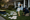 Person kneels on a lawn installing large stork and baby-themed yard signs outside a house.
