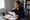 Woman reviews paperwork at a dining table beside a window, with a mug and documents nearby.