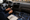A person works on a car dashboard, holding wiring tools beside a removed radio, replacement screen, and trim panels.