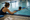 An adult steadies a child practicing a swim stroke in a pool beside a clipboard.