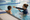 Swimming instructor gestures toward a child holding the pool edge during a lesson in an indoor pool.