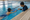 An instructor coaches a swimmer holding a kickboard in an indoor pool.