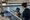 Adult instructor supports a child practicing with a kickboard at the edge of an indoor pool.