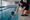 Swim instructor kneels beside an indoor pool, guiding a child practicing swimming at the pool’s edge.