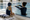 Swim instructor gestures toward the pool while a child listens at the pool’s edge.