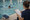 Instructor takes notes on a clipboard as a swimmer practices in an indoor pool.