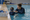 Swim instructor assists a child in the water beside an indoor pool deck.