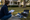 Person crouches with a clipboard beside decorative yard sign pieces on a suburban lawn.