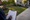 A person writes on a clipboard beside a landscaped yard, house, and concrete driveway.
