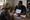 A man in blue scrubs shows documents to a woman seated at a table indoors.