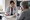 A healthcare professional discusses documents with a gray-haired woman seated at a kitchen table.