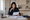 Woman reviews documents at a kitchen table, surrounded by papers, a notebook, and a cup.