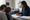 Clinician discusses paperwork with a woman and child seated at an examination room desk.