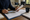Person reviews paperwork and writes beside a property photograph at a wooden table in a living room.