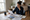 Woman sits at a dining table reviewing paperwork in a bright home kitchen.