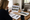 Woman reviews property listings at a kitchen table beside a laptop, notebook, brochures, and coffee.
