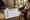 People review a chart and point to entries around a wooden table in a rural setting.