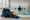 Swim gear rests beside an indoor pool while an instructor works with children in the water.