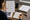 Person compares highlighted documents while taking notes in a notebook beside a coffee mug and magnifying glass.