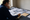 Person wearing glasses reviews printed documents and writes notes at a desk.
