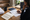Person reviews paperwork and writes notes at a wooden desk beside a laptop, notebooks, and coffee.