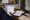 Person reviews and writes on paperwork at a dining table in a kitchen, with a coffee mug nearby.