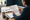 Person reviewing a printed document and taking notes at a desk beside an open notebook and coffee mug.