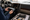 A person holds a car stereo unit beside an open dashboard, wiring harnesses, and tools.