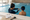 An adult swimmer gestures toward a child in an indoor pool beside a clipboard.