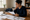 Woman reviews printed documents at a dining table, with a coffee cup and notebook nearby.