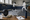 Two fencers practice with foils in a gym, while masks, gloves, equipment, and notes rest on a nearby table.
